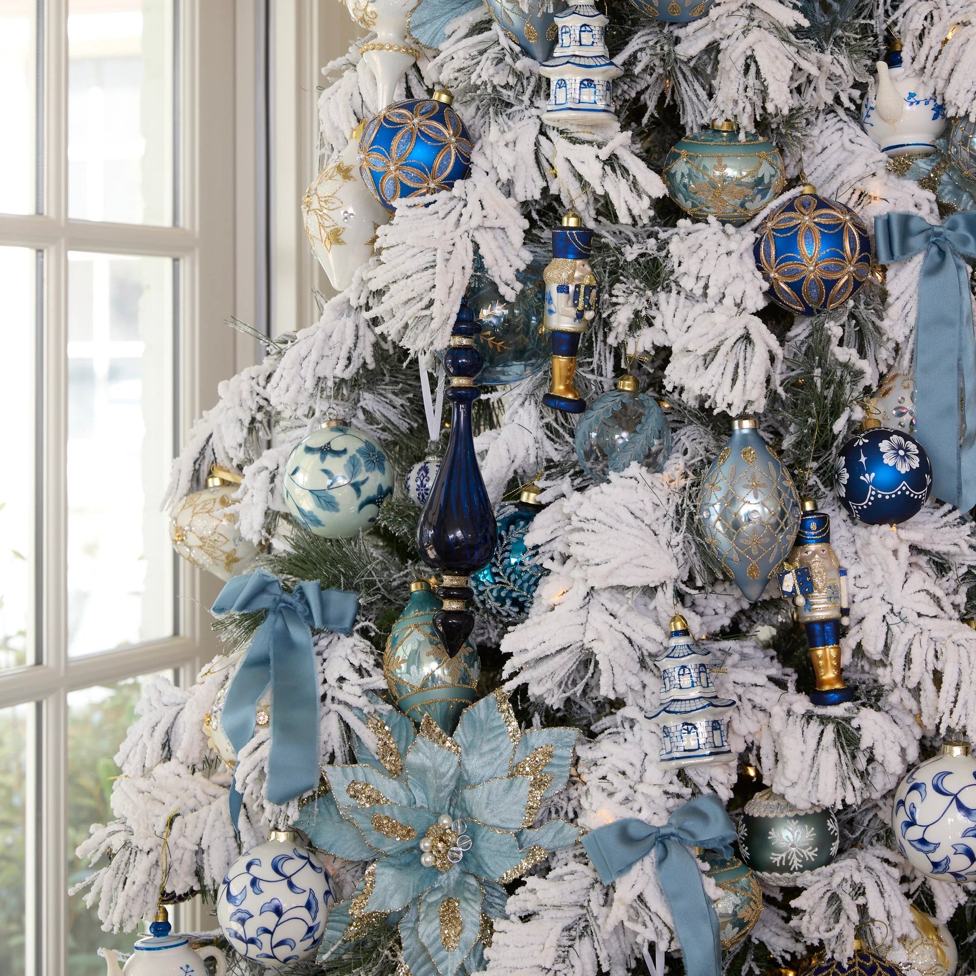 Decorated Christmas tree with blue and silver ornaments in a room with a window.