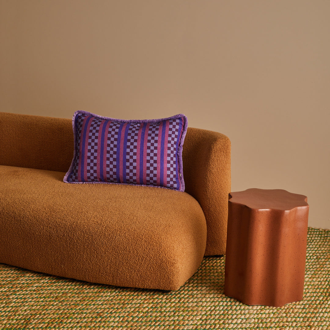 Brown sofa with a striped pillow and matching side table against a beige wall.