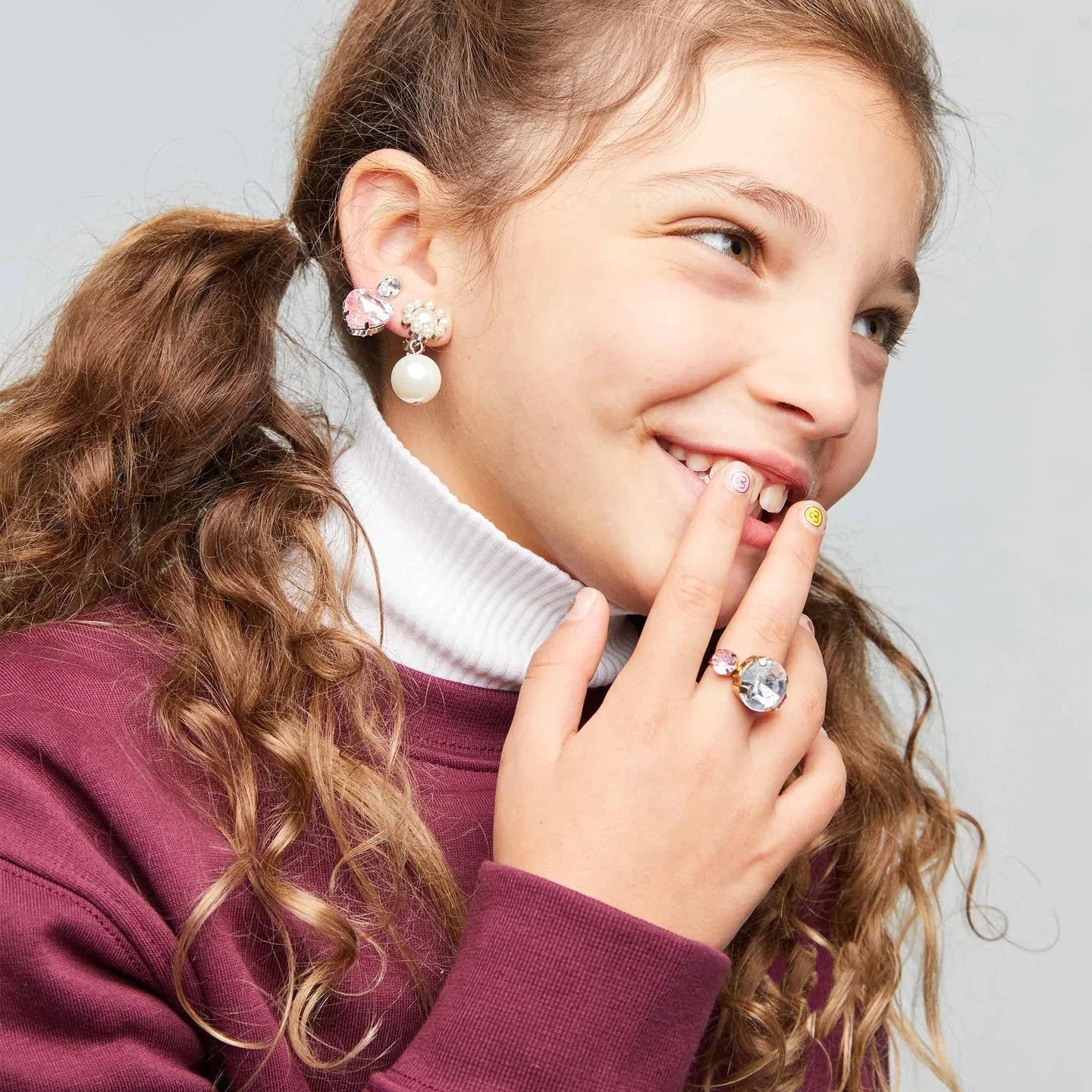 Young girl wearing earrings and a ring with a plain background